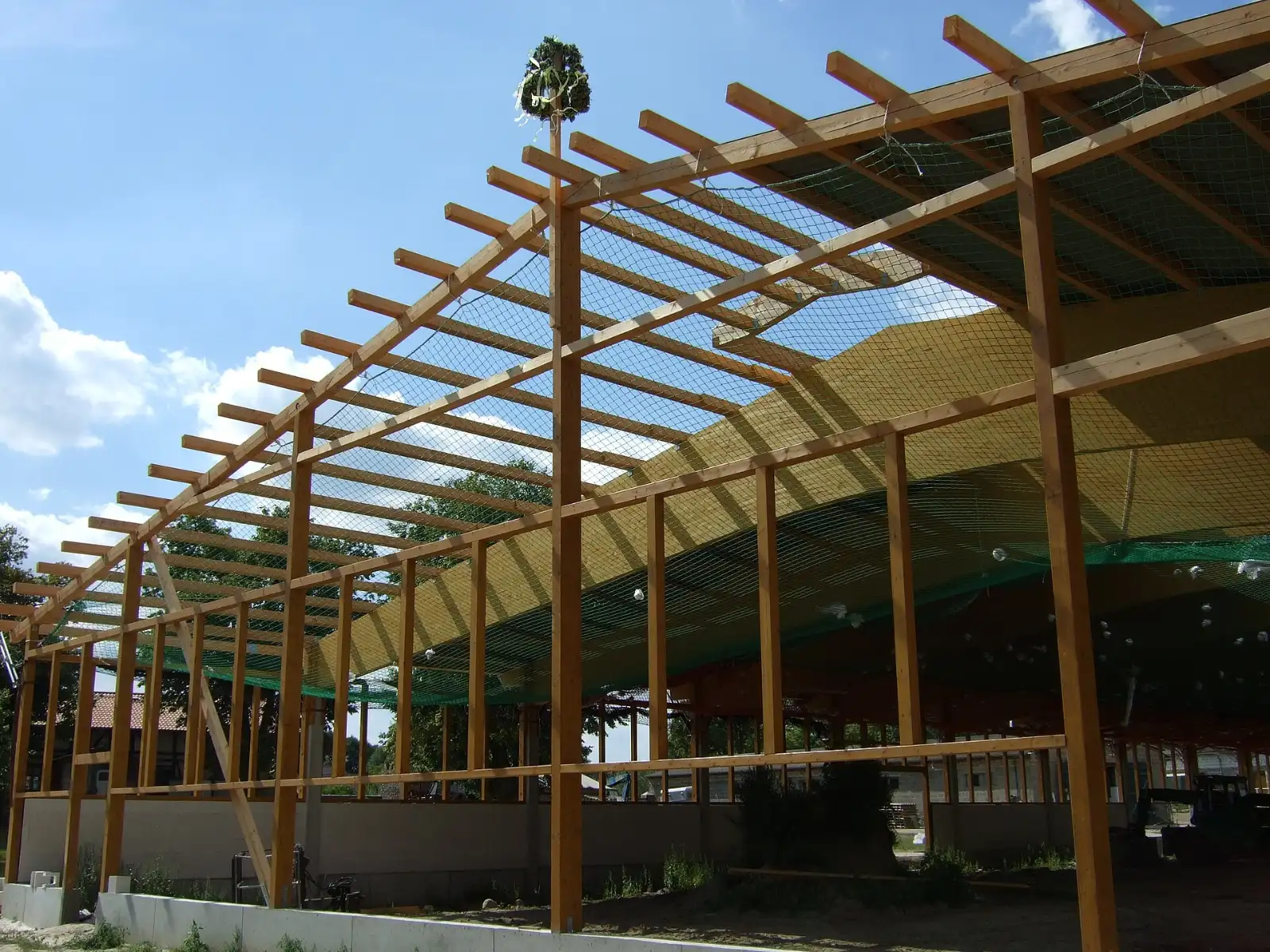 Offene Holzkonstruktion mit Pfosten und Pfetten vor blauem Himmel